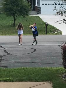 A young boy playing a trumpet follows a young girl down the street. The girl is covering her ears and obviously does not want to listen.